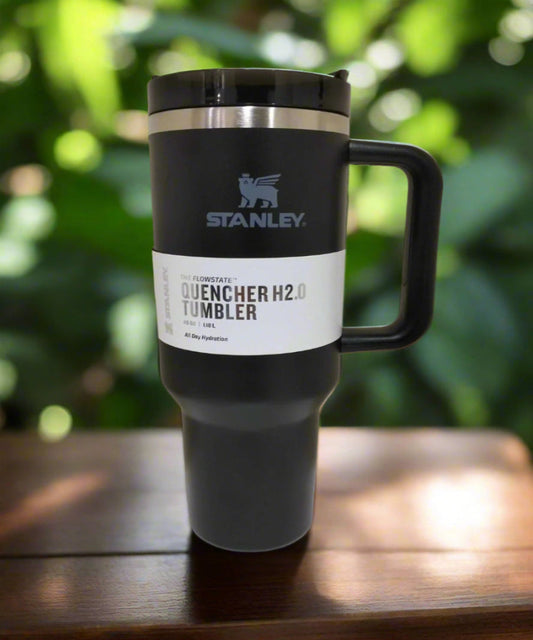 Stanley tumbler with a label on a wooden surface with a blurred green background