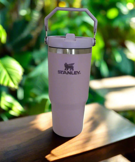 Pink Stanley tumbler on a wooden surface with a green leafy background